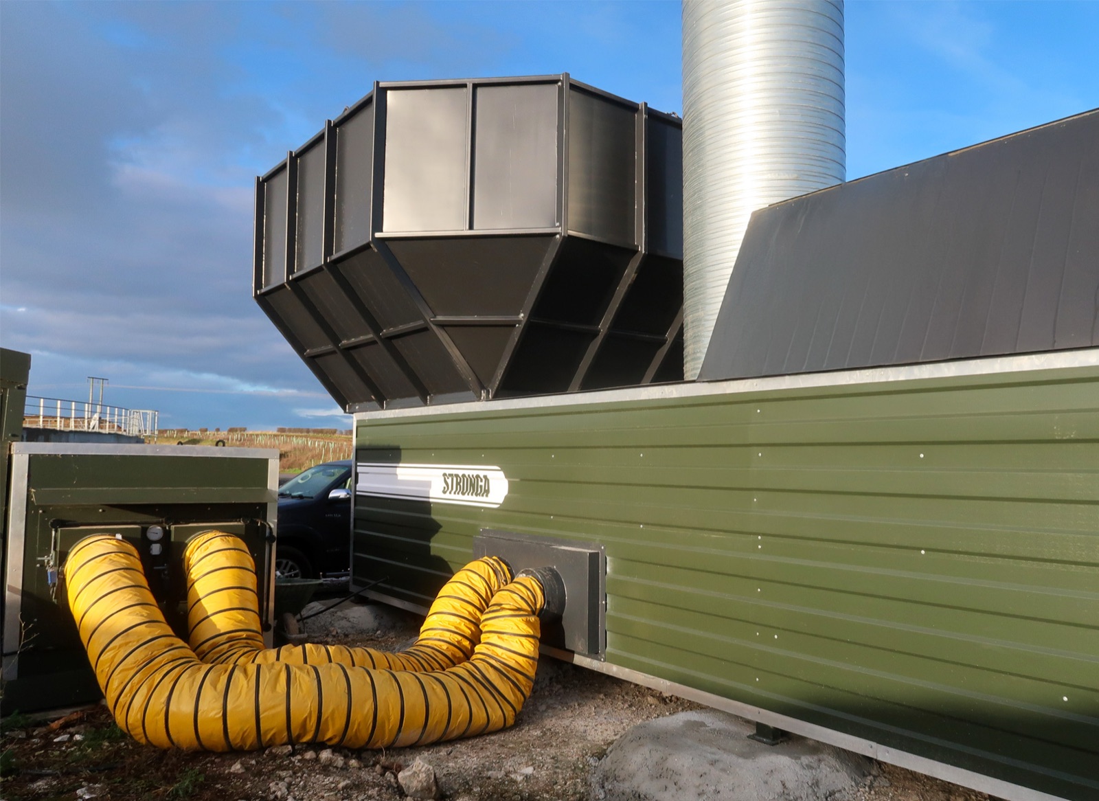 FlowDrya poultry manure dryer connected to chicken house residual heat via yellow ductwork
